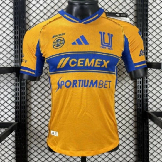 قميص اللاعب نسخة 25/26 لفريق تيغريس UANL باللون الذهبي مع شريط أزرق على الصدر، وشعار الذكرى الخامسة والستين، وقميص Sportiumbet
